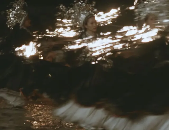 Dancer in a black pleated dress and ornate silver headdress turning through a dark nighttime scene
