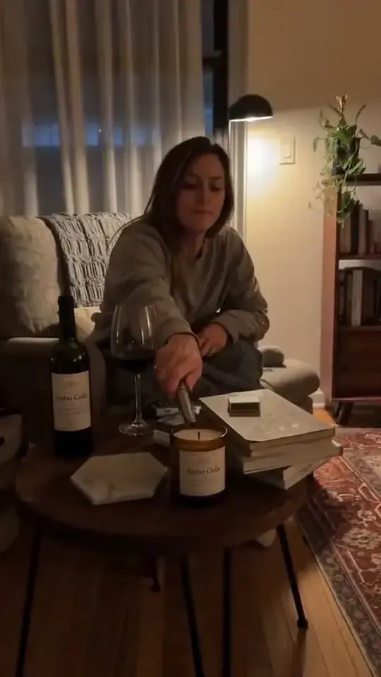 Amber glass candle on a coffee table in a warmly lit apartment with a woman relaxing nearby