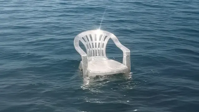 Single white plastic chair encrusted with small shells floating alone in open blue sea