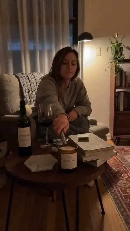 Amber glass candle on a coffee table in a warmly lit apartment with a woman relaxing nearby