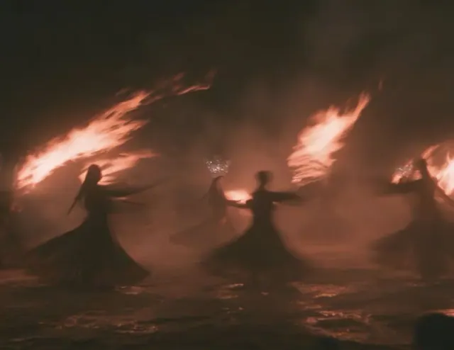 Women dancing with torches at night, their dark silhouettes framed by warm firelight