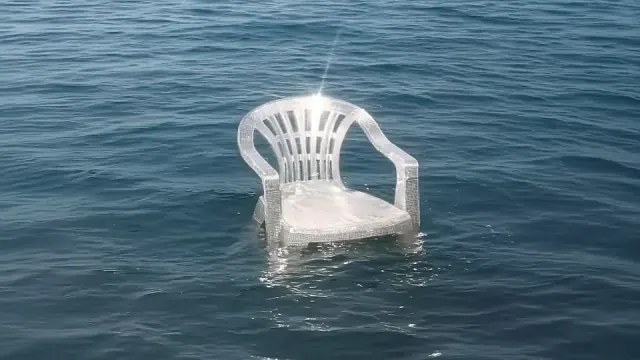 Single white plastic chair encrusted with small shells floating alone in open blue sea