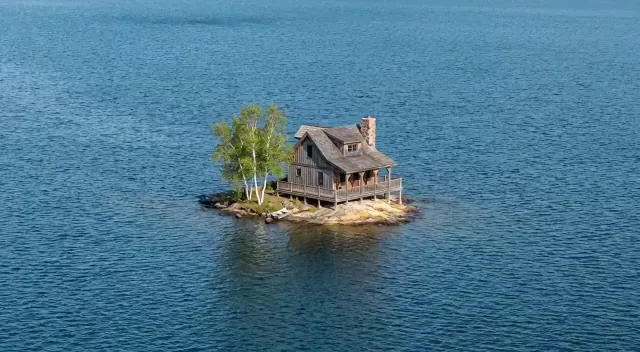 Rustic timber cabin and birch trees on a tiny rocky island surrounded by blue lake water
