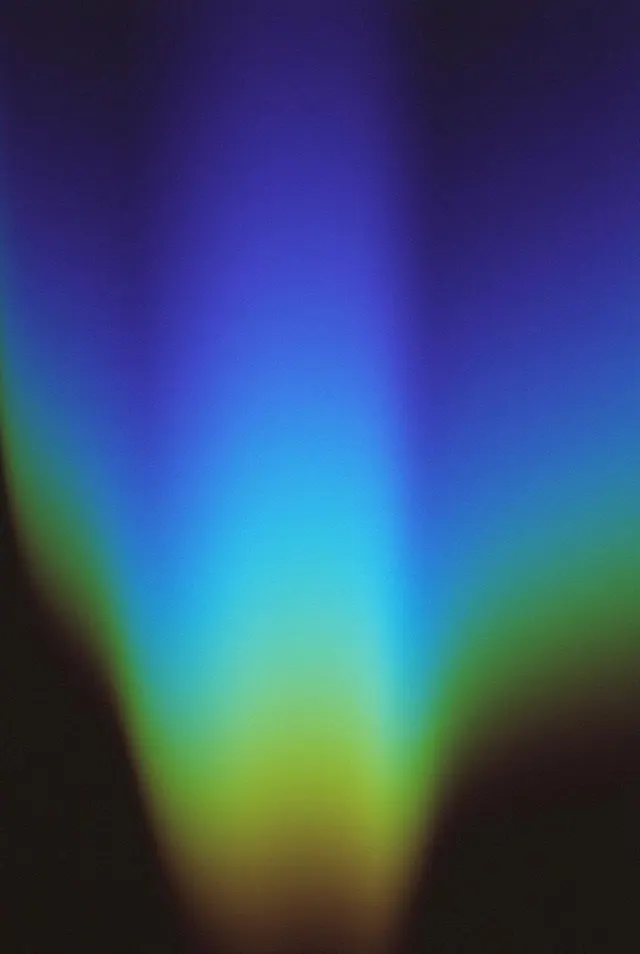 A blurred fan of indigo, cyan and green light narrows toward a yellow green base on charcoal.