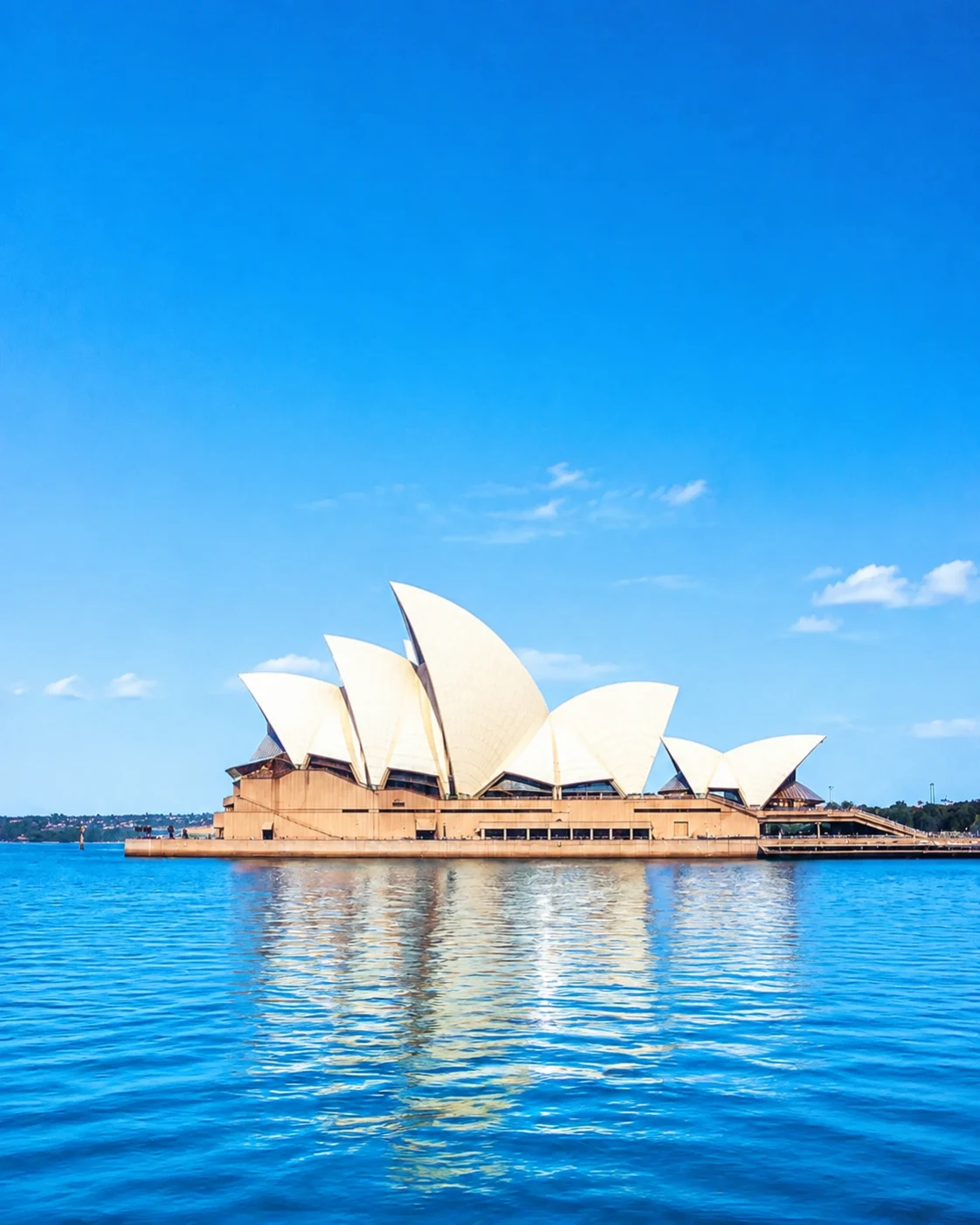 Sydney Opera House in bright daylight above blue, choppy harbour water